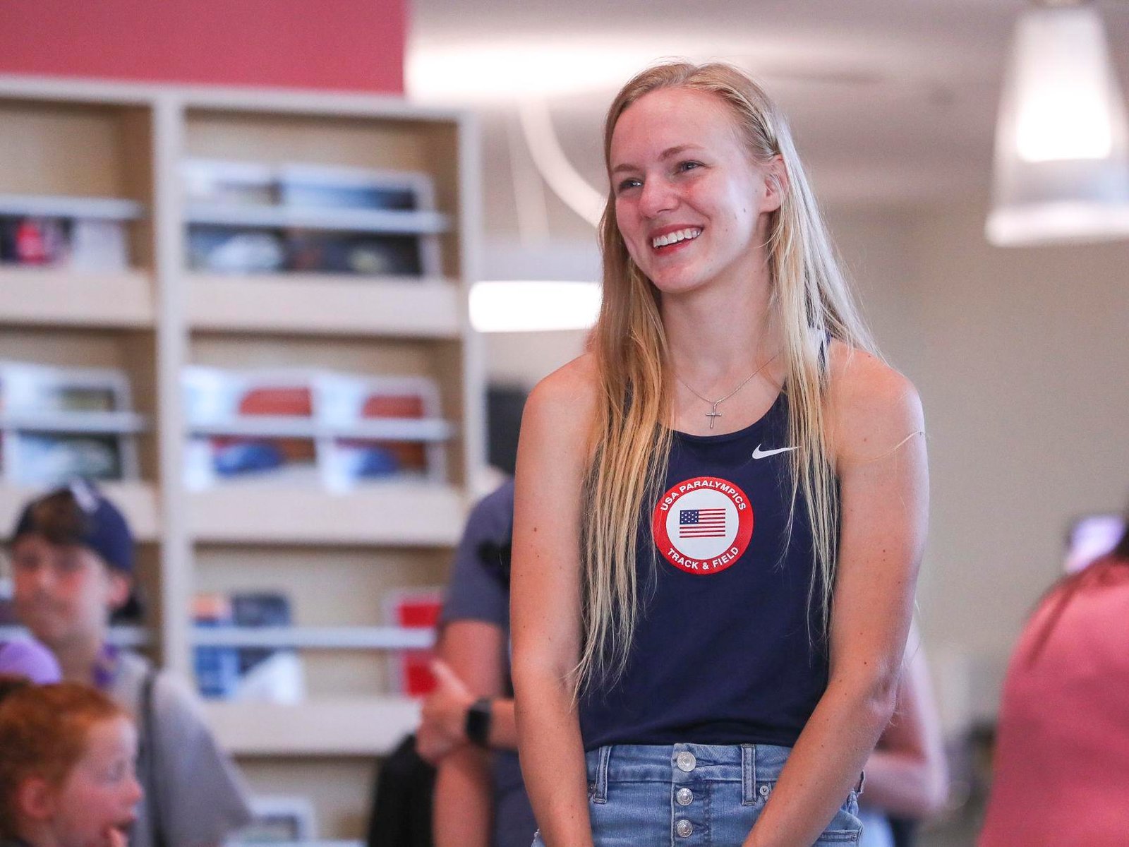 Jessica, wearing a navy blue USA tank top over her jeans, smiling while listening to someone speaking